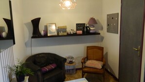 Un salon avec un canapé en cuir foncé, une chaise en bois, une petite table ronde et une bibliothèque contenant divers objets décoratifs.
