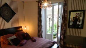 Une chambre avec un grand lit, un luminaire suspendu, une porte-fenêtre coulissante donnant sur un balcon et un miroir au mur.
