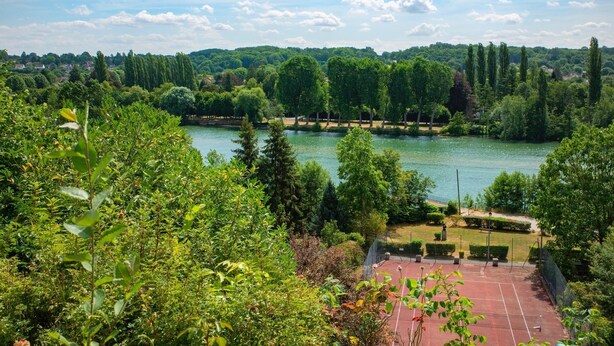 A tennis court surrounded by lush greenery and a lake. - La Petite Affolante, charming residence in Samois Sur Seine (Samois Sur Seine)
