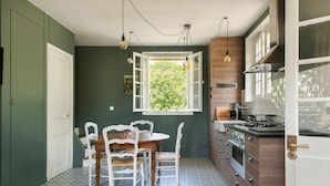 A compact kitchen with a dining area, featuring a wooden table and chairs, a window with a view of greenery, and modern appliances. - La Petite Affolante, charming residence in Samois Sur Seine (Samois Sur Seine)