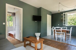Una stanza accogliente con un tavolo in legno, sedie bianche, un televisore e una porta che dà su un balcone.
