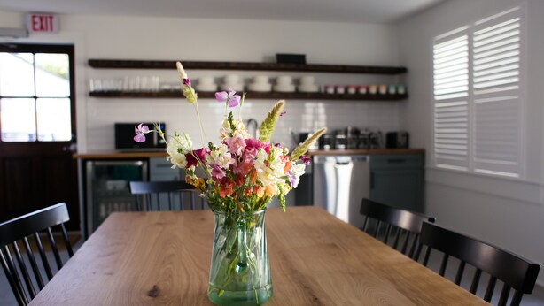 Ein Holztisch mit einer Glasvase mit Blumen in einer modernen Küche mit weißen Schränken und einem eingebauten Backofen.
