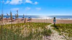 A beach with sand, grass, and a sign.