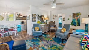 A spacious living room with a ceiling fan, a dining area with a table and chairs, and a kitchen area with cabinets and a microwave.