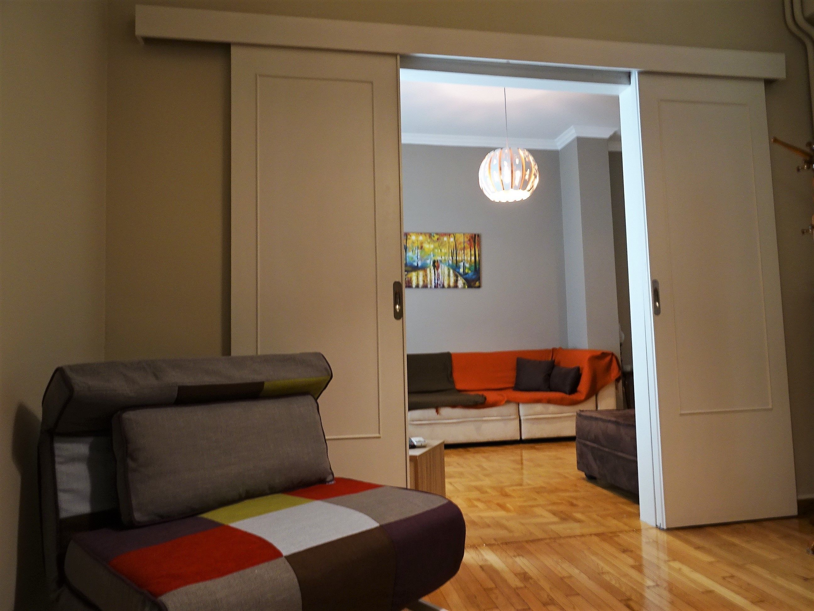 A room with a sofa, a colorful chair, and a painting on the wall.
