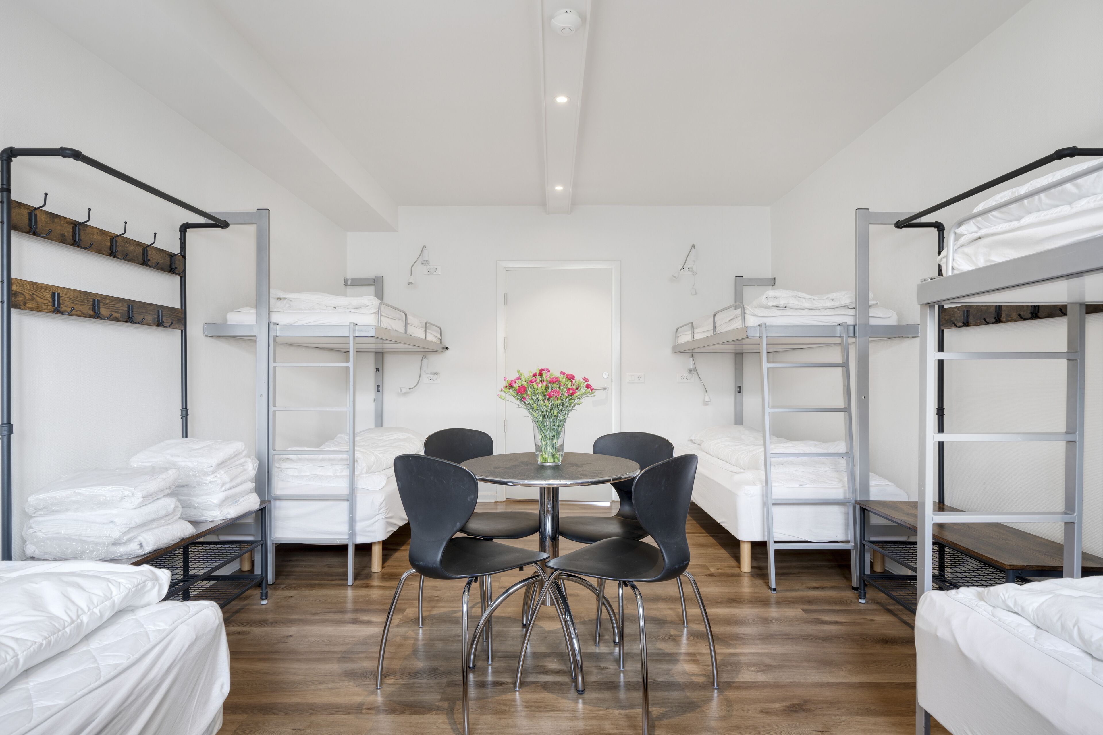 Un dormitorio con literas, una mesa redonda con sillas y un florero con flores.