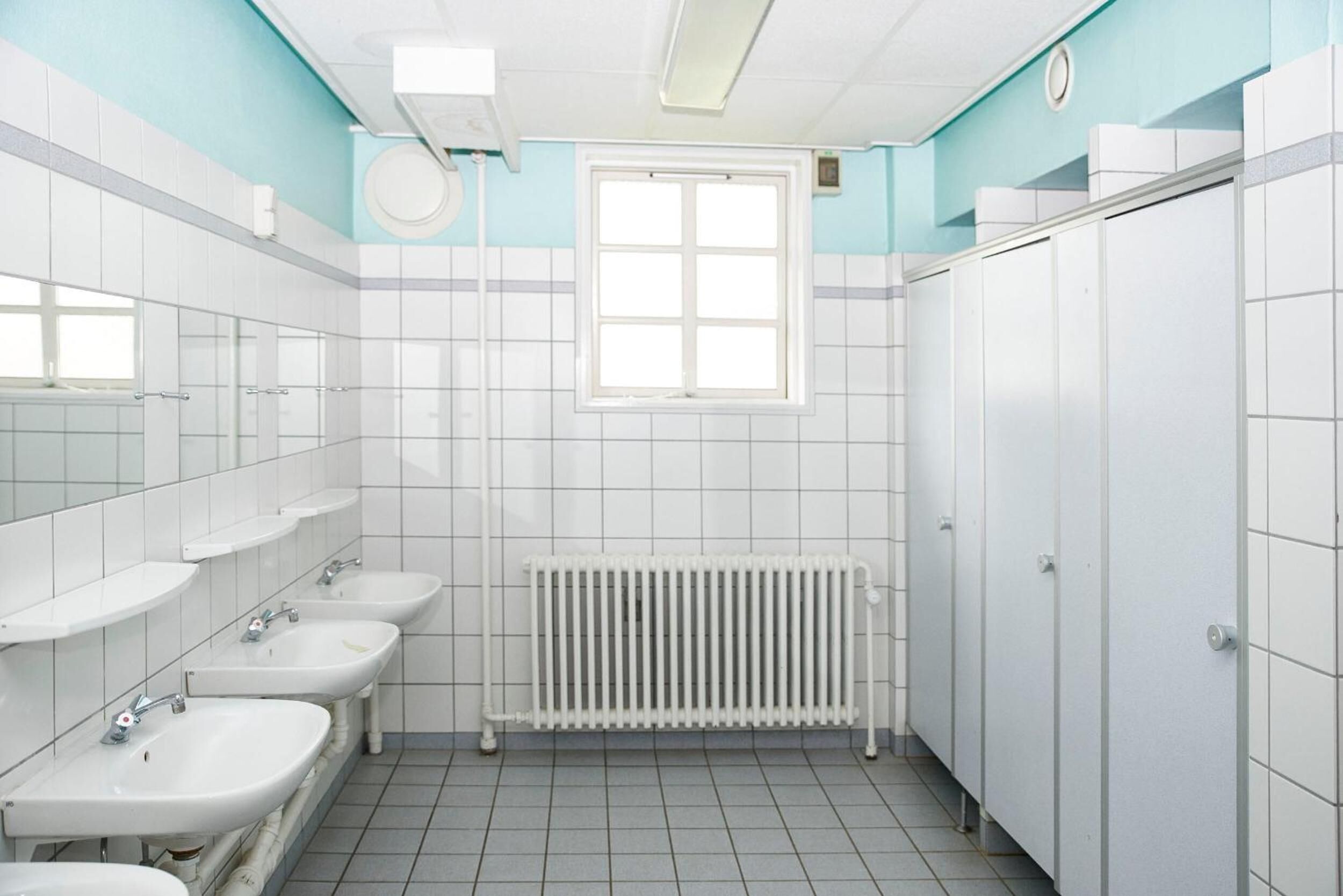 Un baño con lavamanos blancos, una ventana y un radiador.