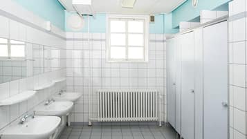 Un baño con lavamanos blancos, una ventana y un radiador.