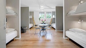 A modern, well-lit room with bunk beds, a round dining table with chairs, and a radiator. - Kragsbjerggaard Vandrerhjem (Odense)