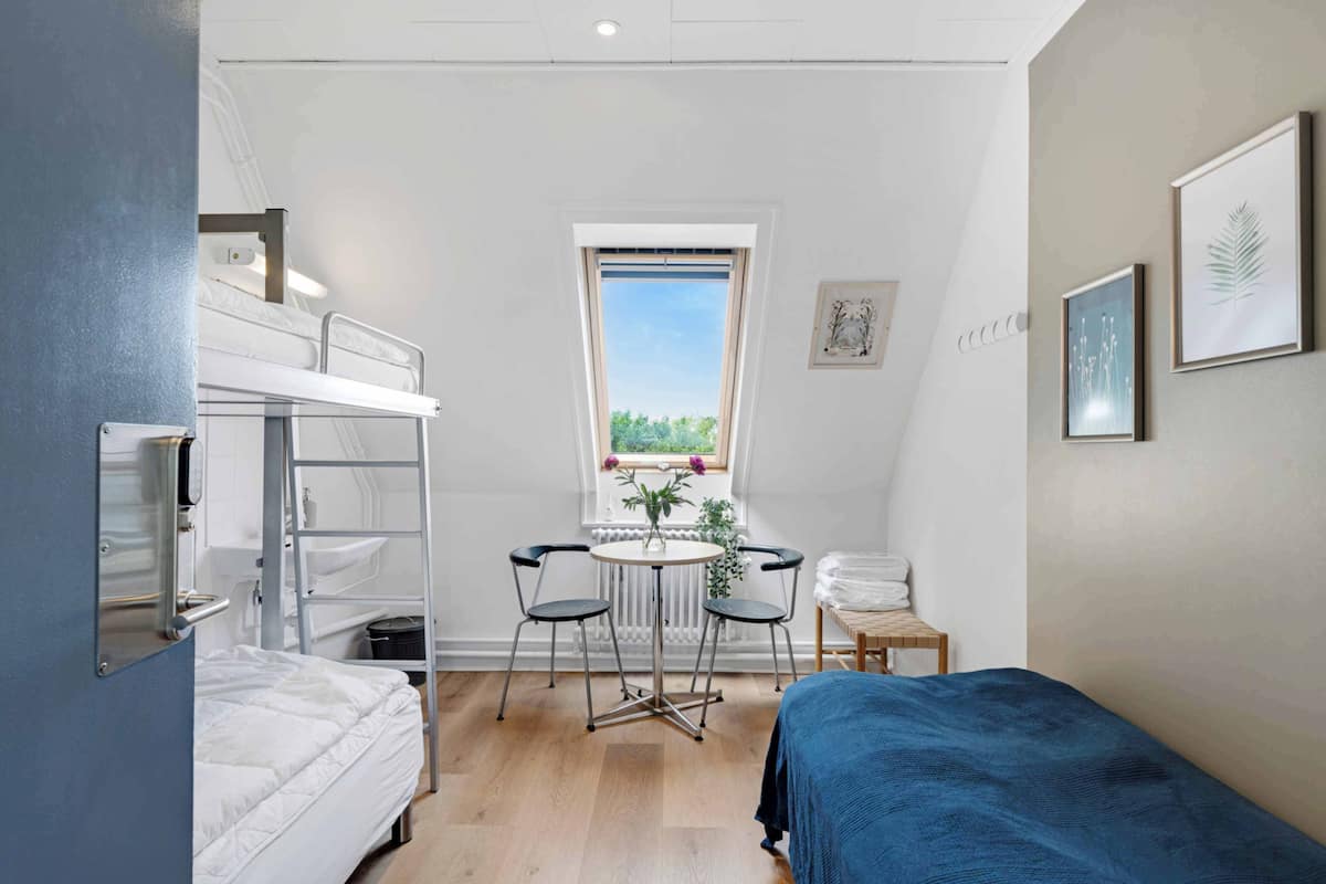 Una habitación compacta con literas, una pequeña mesa redonda con sillas, un ventanal con vistas y una cama con cubrecama azul.