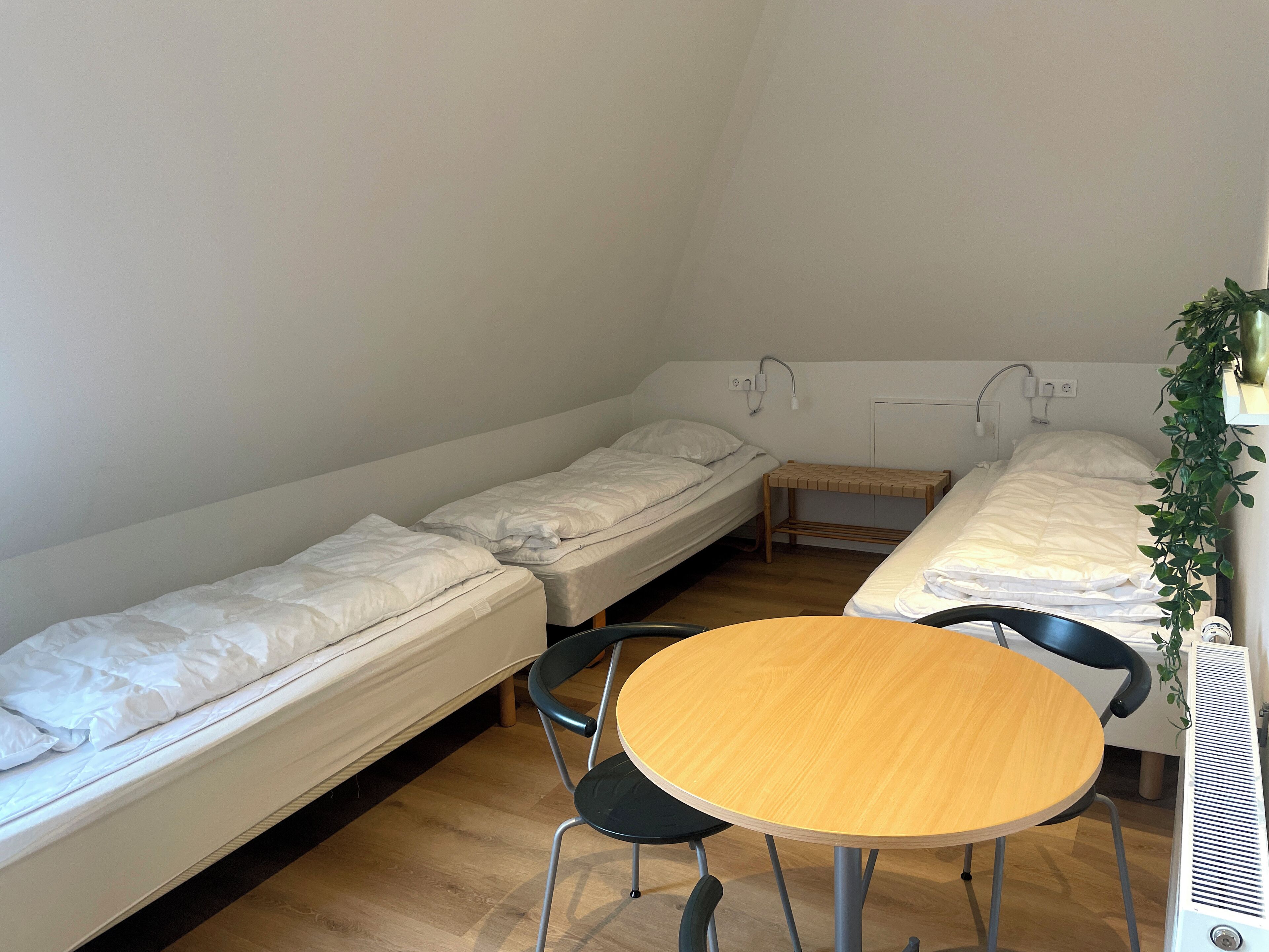 A small, compact room with two single beds, a wooden table, and chairs.