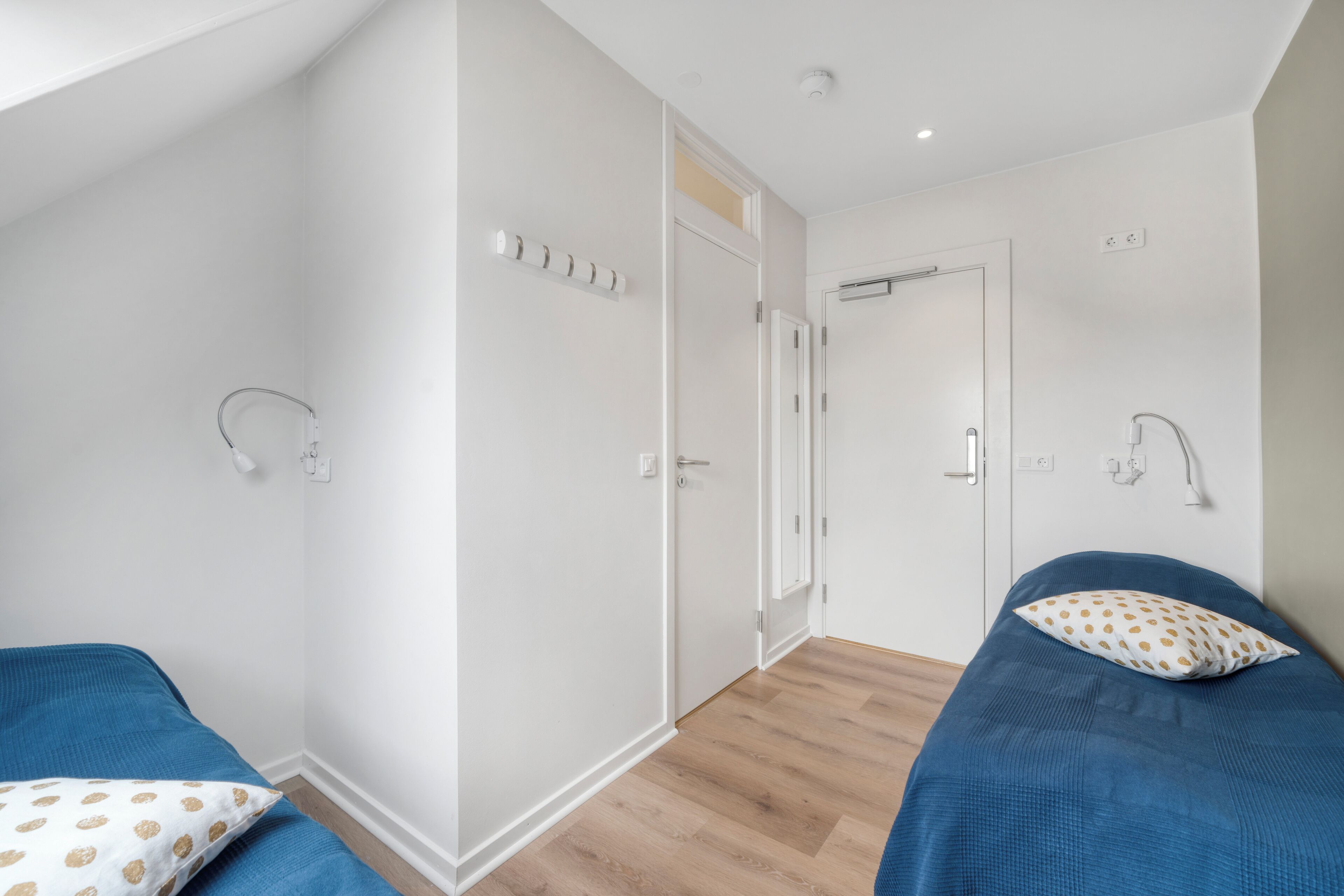 Een slaapkamer met twee bedden, witte muren, houten vloer en een inloopkast met spiegel.