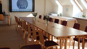 A conference room with a long table, chairs, a screen displaying 'KRAGSBJERGAARD', and skylights. - Kragsbjerggaard Vandrerhjem (Odense)