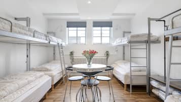 A dormitory room with bunk beds, a round table with chairs, and a vase with flowers.