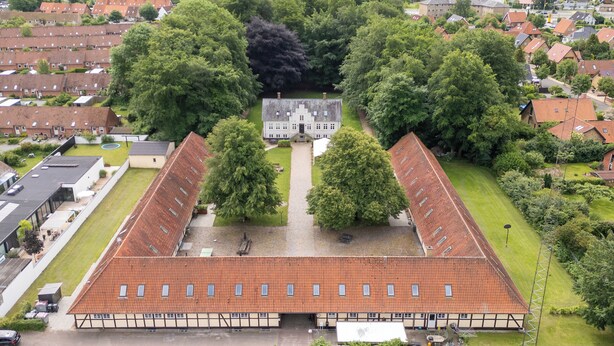 A large, rectangular building with a tiled roof, surrounded by lush greenery and residential buildings. - Kragsbjerggaard Vandrerhjem (Odense)