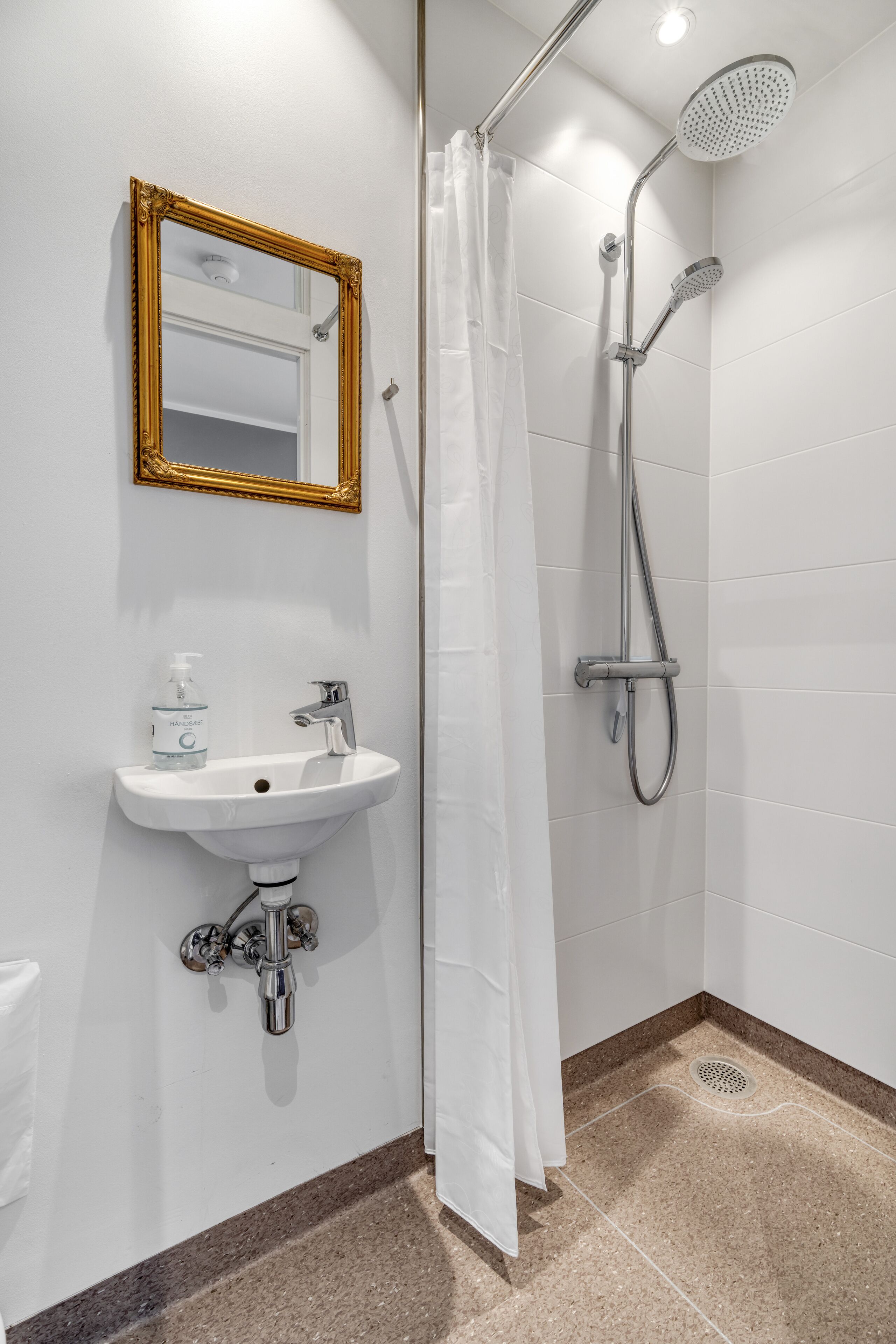 Un baño con un lavamanos blanco, un espejo con marco dorado y una ducha con cabezal de ducha manual.