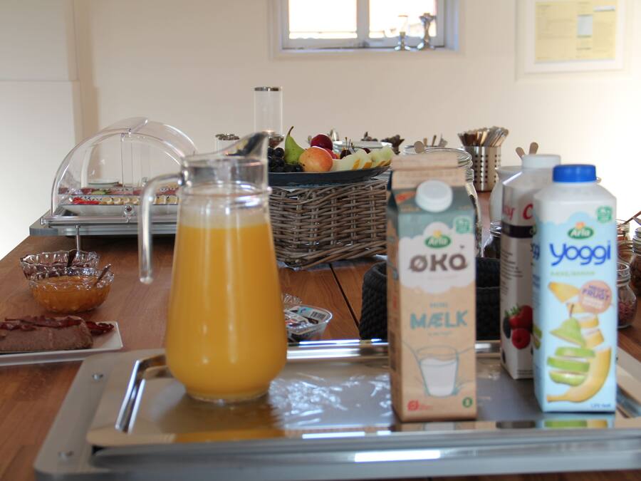 Un bufé de desayuno con diversas opciones de alimentos y bebidas, incluyendo una jarra de jugo de naranja, un cartón de leche y una jofaina de yogur.