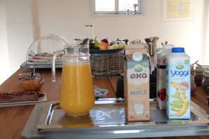 A breakfast buffet with various food items and beverages, including a pitcher of orange juice, a carton of milk, and a jug of yogurt.