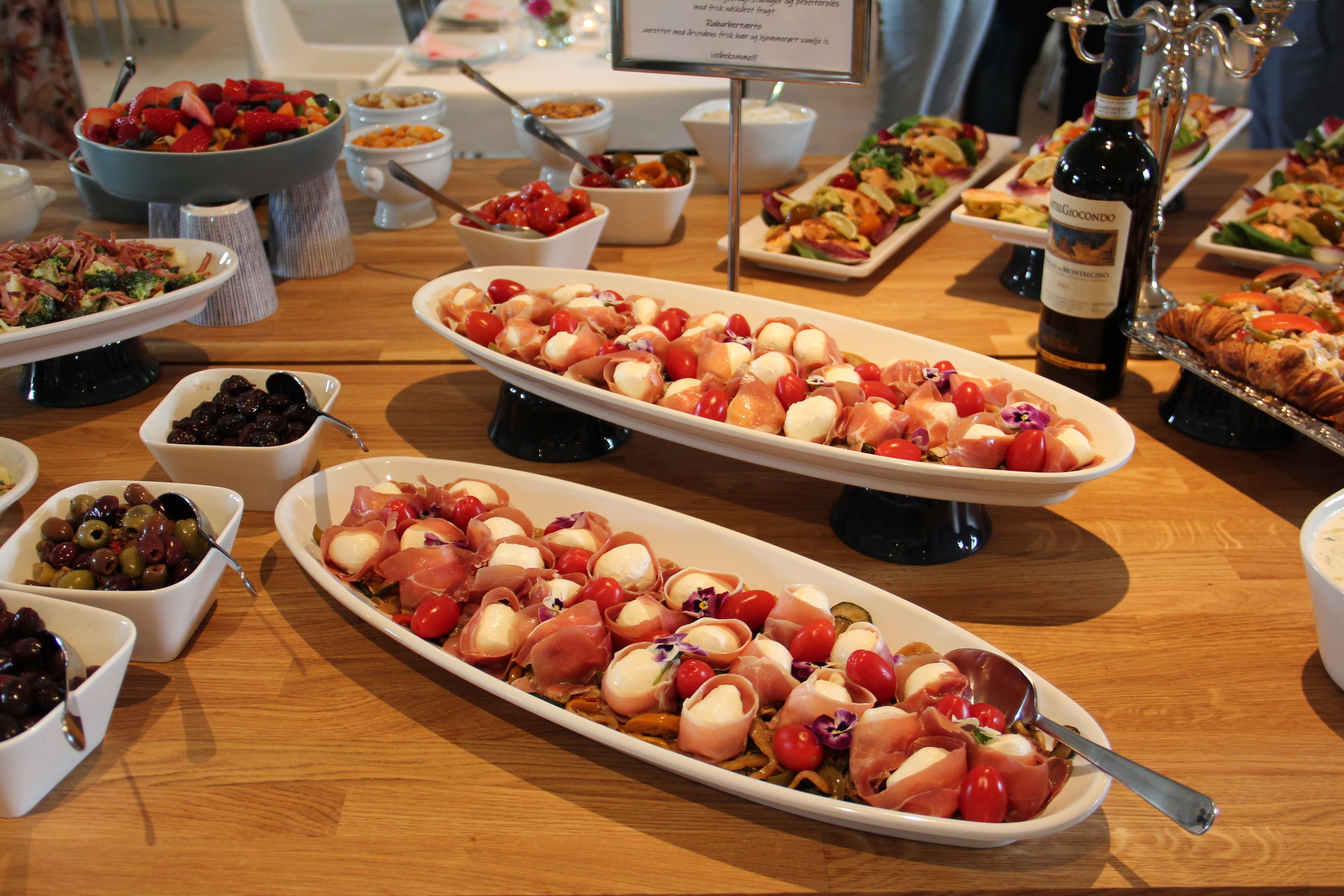 Variedad de fuentes de comida sobre una mesa de madera, con platos que incluyen aceitunas, tomates y queso.