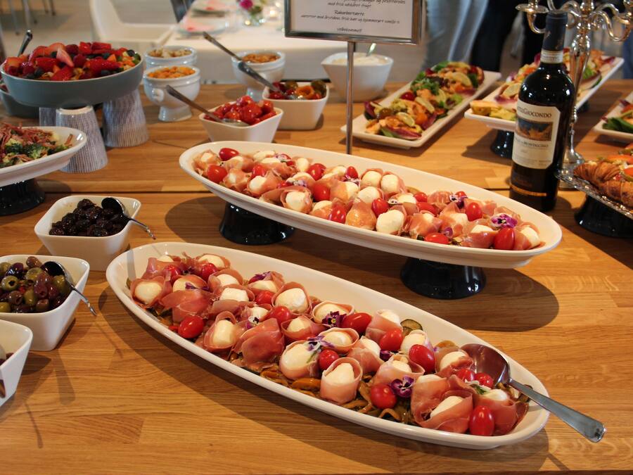 Variedad de fuentes de comida sobre una mesa de madera, con platos que incluyen aceitunas, tomates y queso.