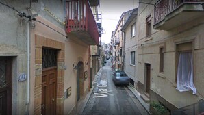 A narrow street with buildings on both sides, a car parked on the right, and a visible street sign. - Crocco d'oro (Caltavuturo)