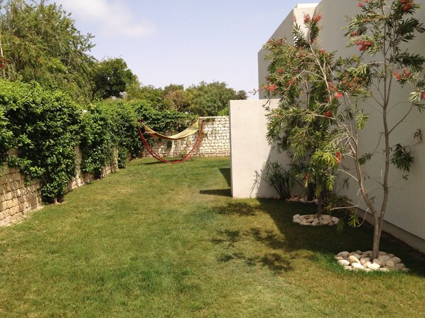 Un jardín cuidado con una hamaca, un muro de piedra y diversas plantas.