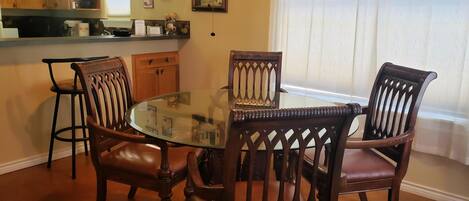 Un espace repas avec une table à plateau de verre, entourée de chaises en bois dont les dossiers présentent des motifs complexes.
