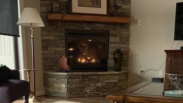 A living room with a stone fireplace, a television mounted above it, a floor lamp, and a sofa with a cushion.