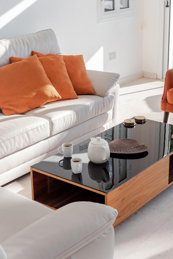 A modern living room with a white sofa, orange cushions, and a glass coffee table with a teapot and cups.