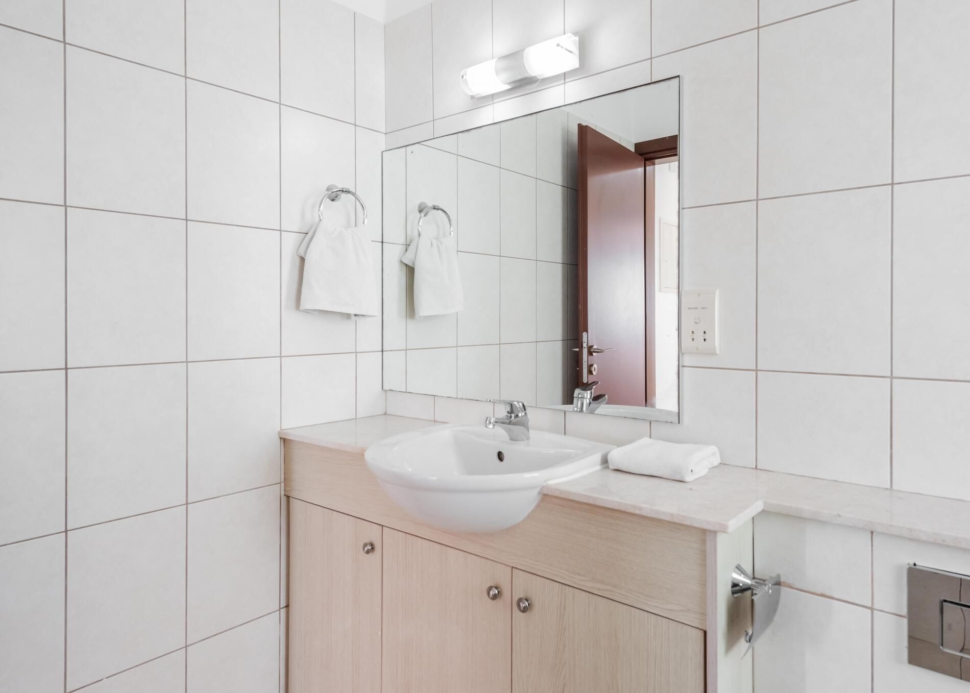 Ein modernes Badezimmer mit weißen Fliesen, einem großen Spiegel, einem Waschbecken und Holzschränken.