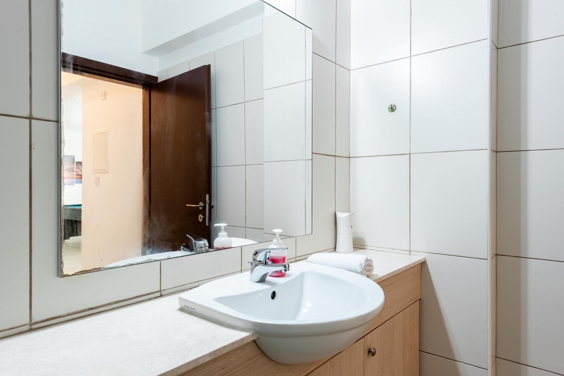 Ein modernes Badezimmer mit großem Spiegel, weißen Fliesen, einem weißen Waschbecken und einer Holzausstattung.
