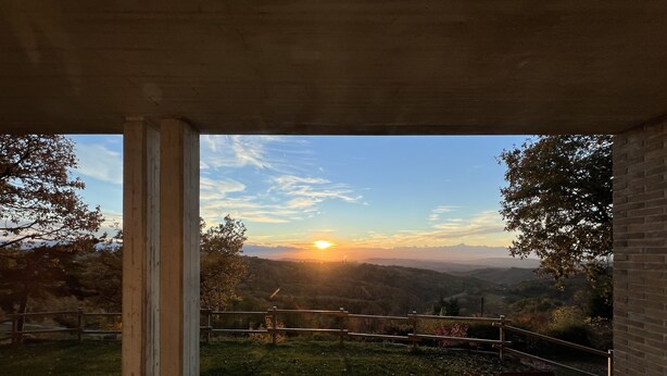 A view from a covered outdoor area with a glass table and chairs, overlooking a hilly landscape and a sunset. - The paradise of relaxation, villa in the Langhe with panoramic views (Lequio Berria)