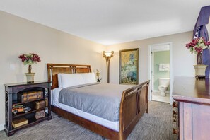 Ein Schlafzimmer mit einem hölzernen Bett, einem Nachttisch mit Lampe, einer Kommode und einem kleinen Regal mit Antiquitäten.