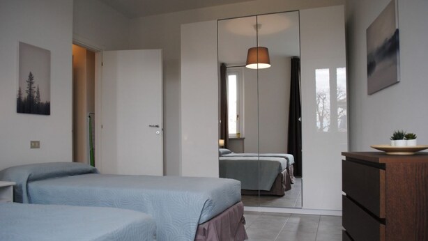 A modern bedroom with two beds, a wardrobe, a dresser, and a mirror.