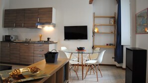 A modern kitchen with wooden cabinets, a flat-screen TV, and a dining area with a glass table and white chairs.