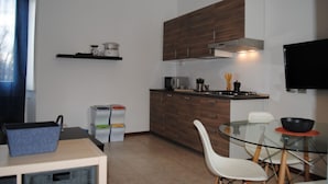 A compact kitchen with wooden cabinets, a gas stove, a microwave, and a small dining area with a glass table and white chairs.