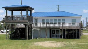A two-story building with a blue roof and a covered area with a balcony. - Pardners - Beachfront  - Island Realty (Grand Isle)