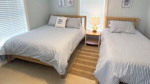 A bedroom with two beds, a nightstand, and a lamp. - Pardners - Beachfront  - Island Realty (Grand Isle)