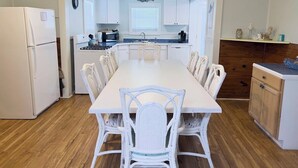 A compact kitchen with white cabinetry, a dining table with white chairs, and a wooden floor. - Pardners - Beachfront  - Island Realty (Grand Isle)