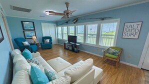 A spacious living room with a white sofa, teal cushions, a wooden floor, and a ceiling fan. - Pardners - Beachfront  - Island Realty (Grand Isle)