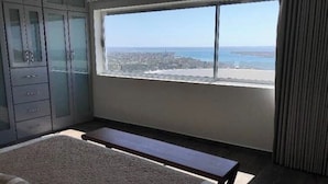 A bedroom with a large window offering a view of the beach and cityscape. - Master Penthouse lujo y comodidad (La Paz)