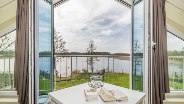 A room with a large window offering a view of a lake and grassy area.