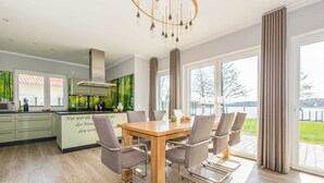 A modern kitchen with a dining area, large windows, and a view of the outdoors.