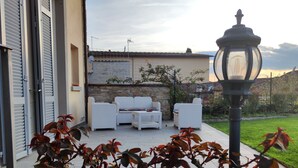 An outdoor seating area with white wicker furniture, a stone wall, and a lamp post.