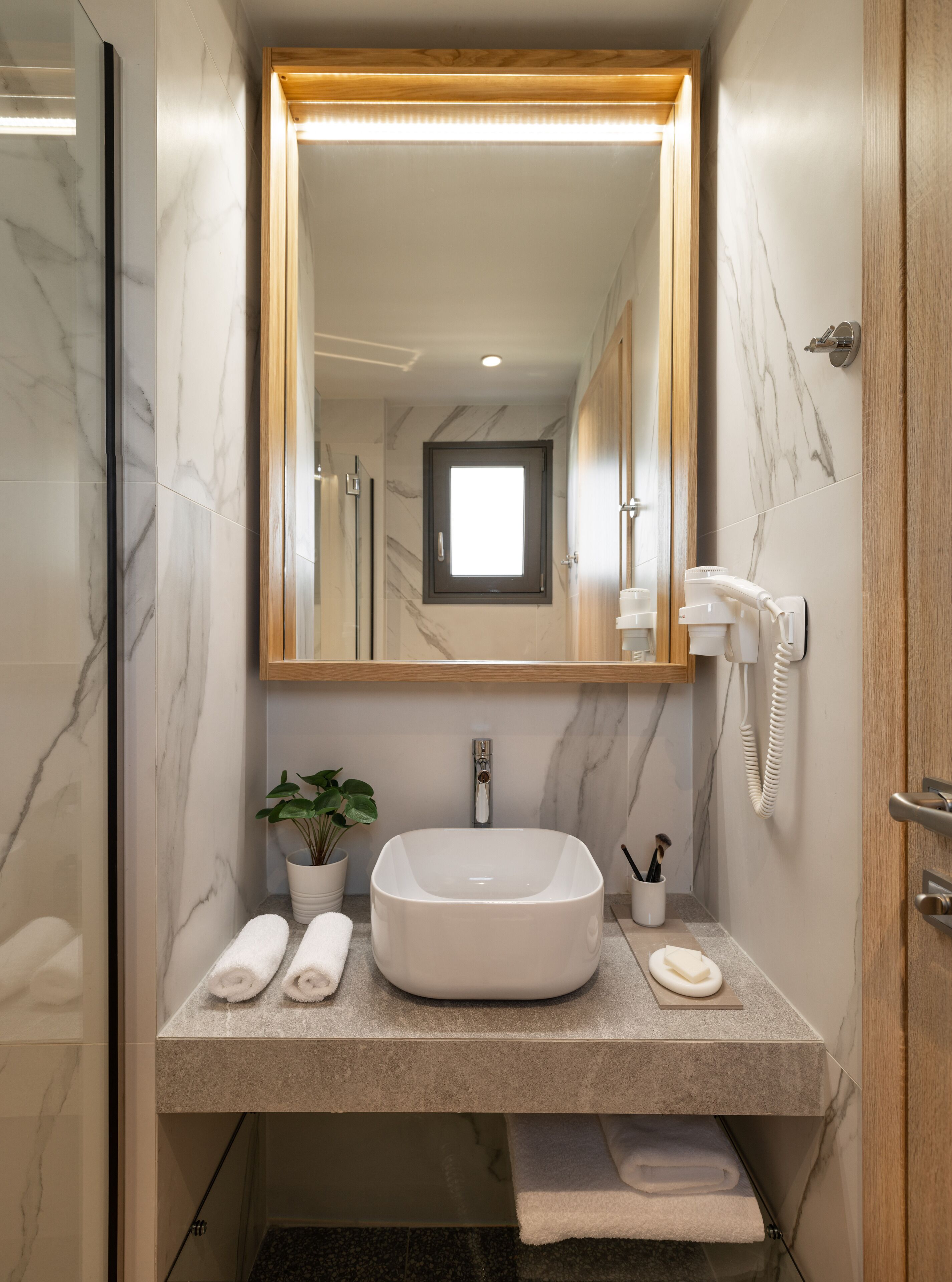 A bathroom with a large mirror, a sink, a towel rack, a potted plant, and a telephone.