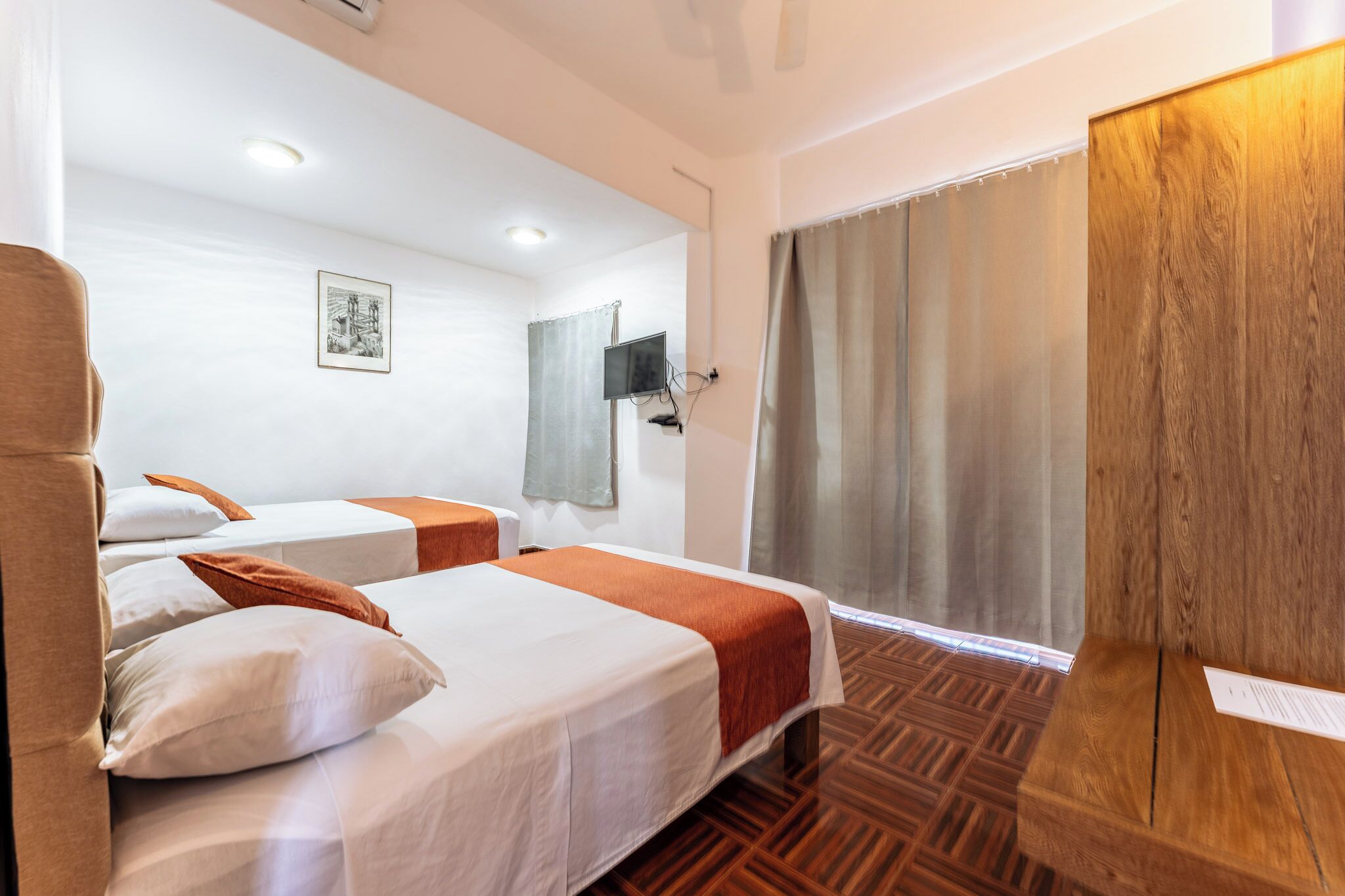 Een hotelkamer met twee bedden, een televisie, een houten garderobe en een raam met gordijnen.