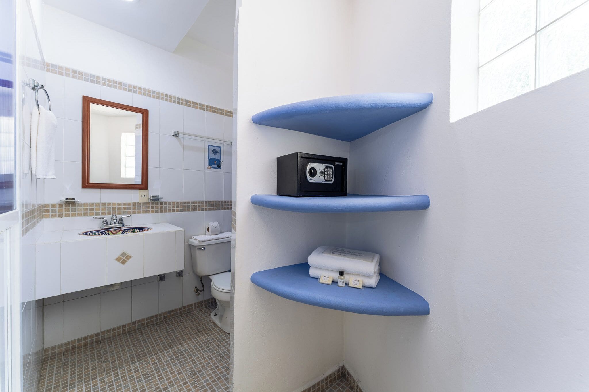 Un baño con un lavabo blanco, un espejo, un inodoro y estantes azules con artículos de aseo.
