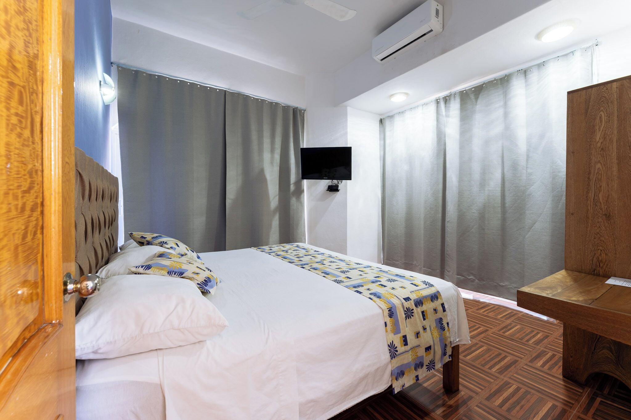 Habitación de hotel con cama, cortinas, televisión y un escritorio de madera.