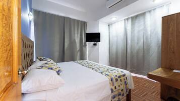 Habitación de hotel con cama, cortinas, televisión y un escritorio de madera.