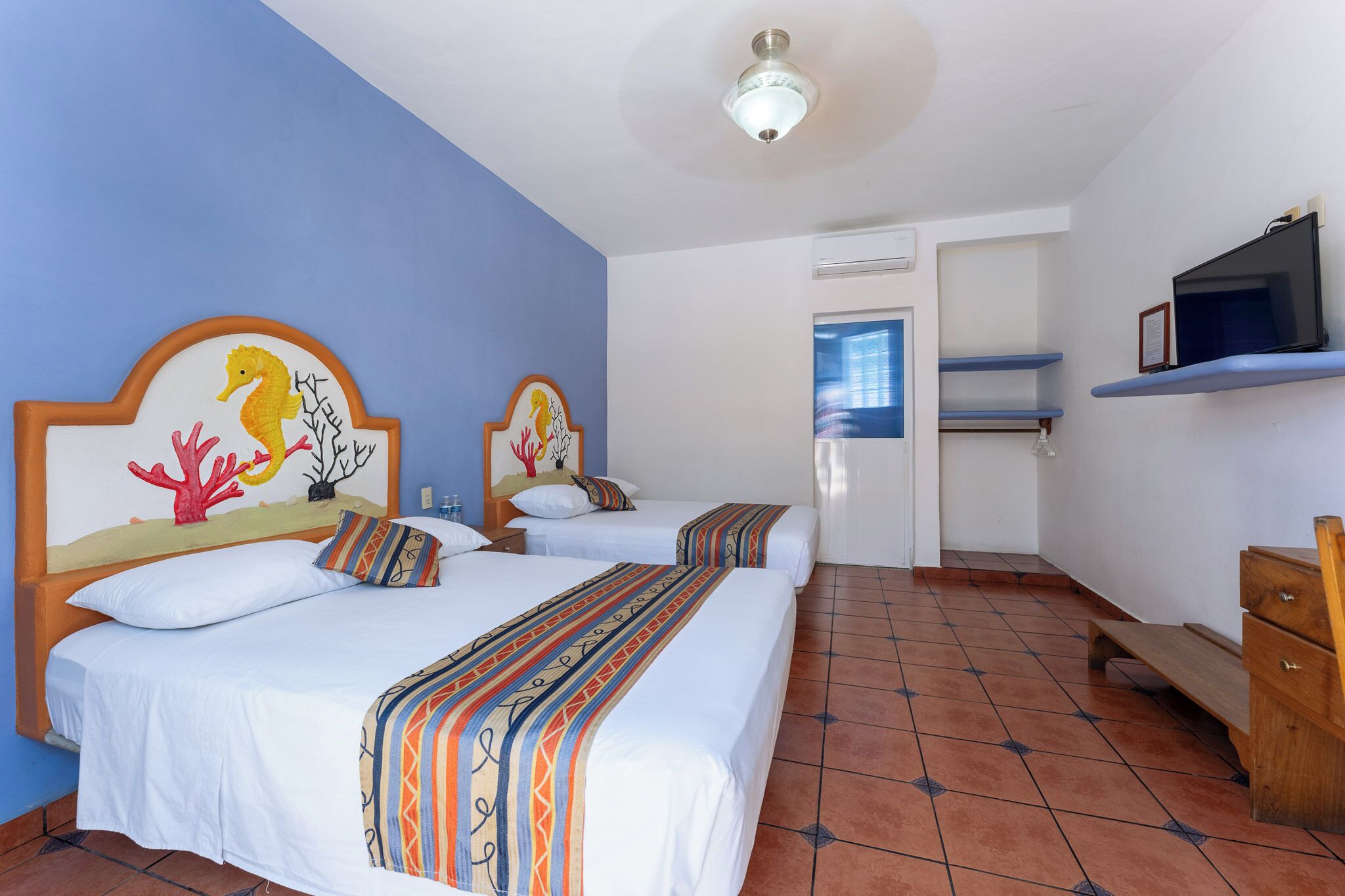 Habitación de hotel con dos camas, televisor, minibar y baño visible a través de una puerta abierta.